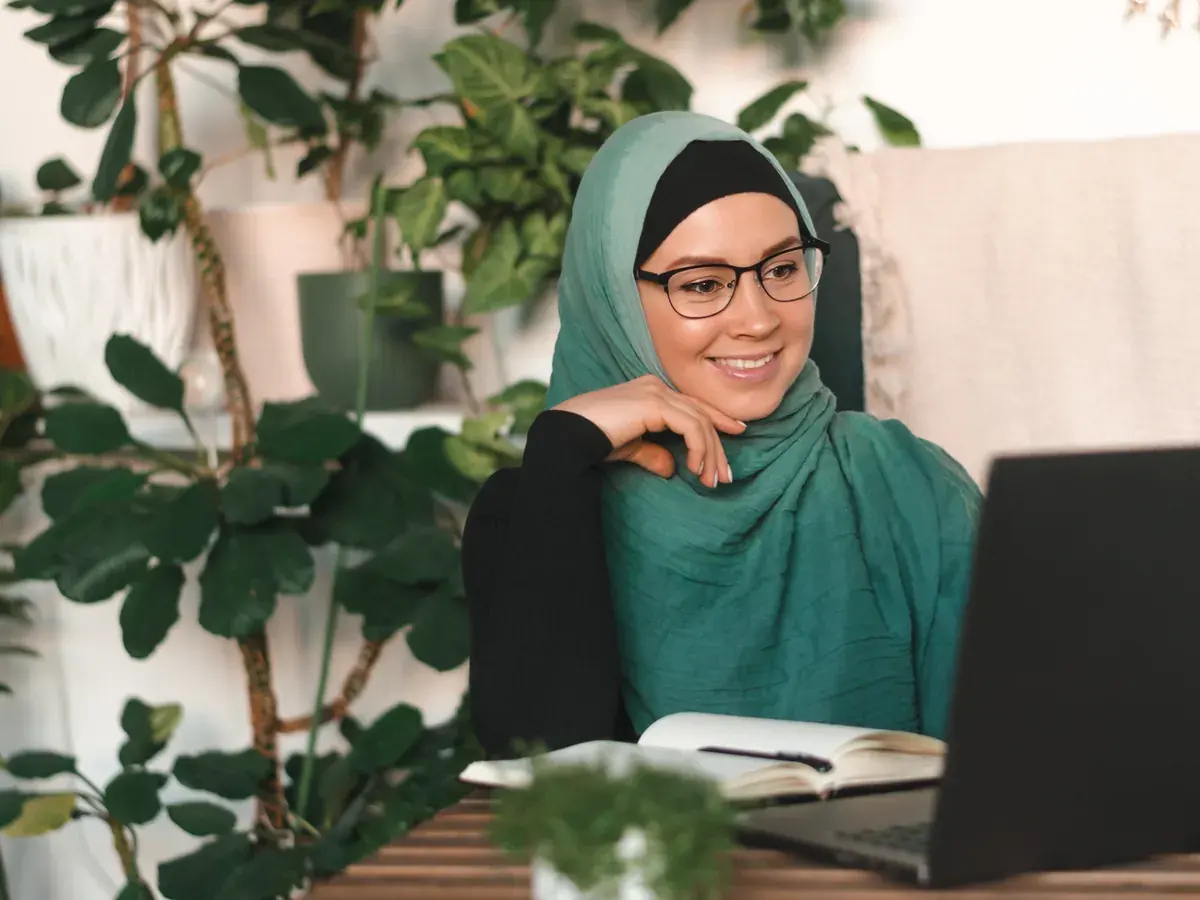 Pekerja remote Indonesia berhijab di meja kerja rumah, tersenyum