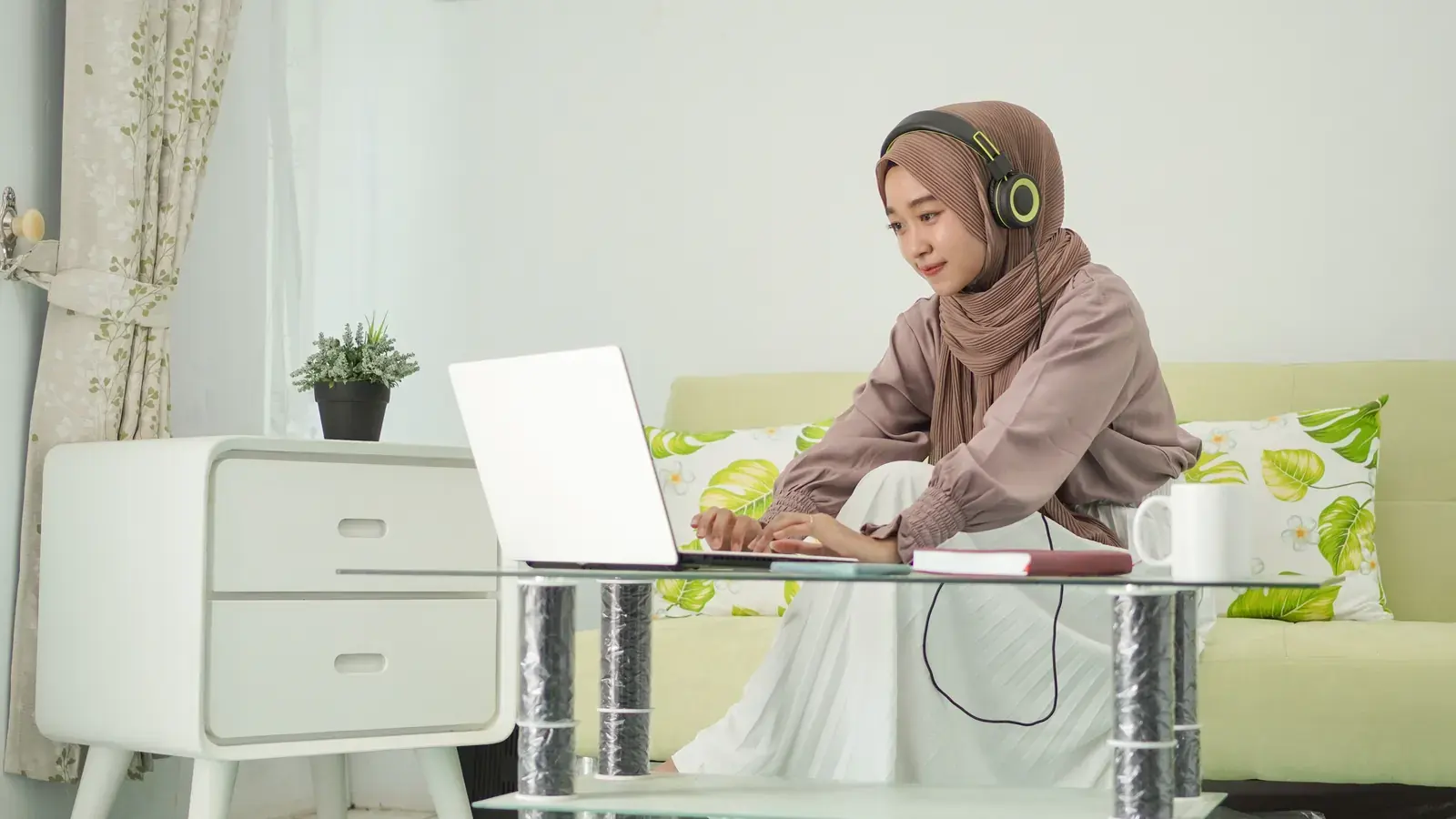 An Indonesian virtual assistant working at a laptop at home, wearing headphones.