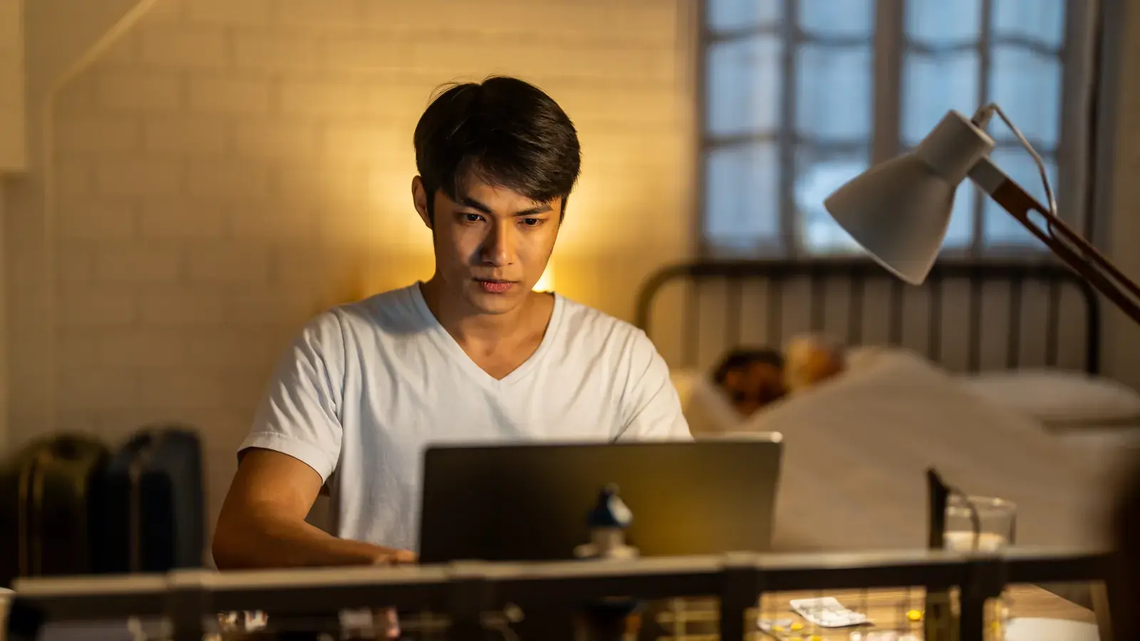 Pekerja remote Indonesia sedang bekerja dengan laptop di rumah pada malam hari.