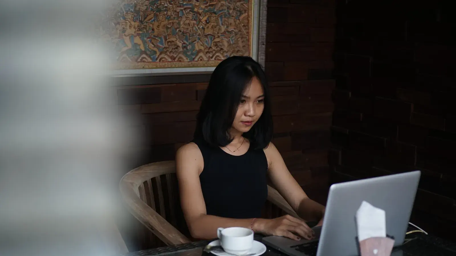 Perempuan Indonesia sedang mengetik CV di laptop, dengan lukisan batik di dinding.