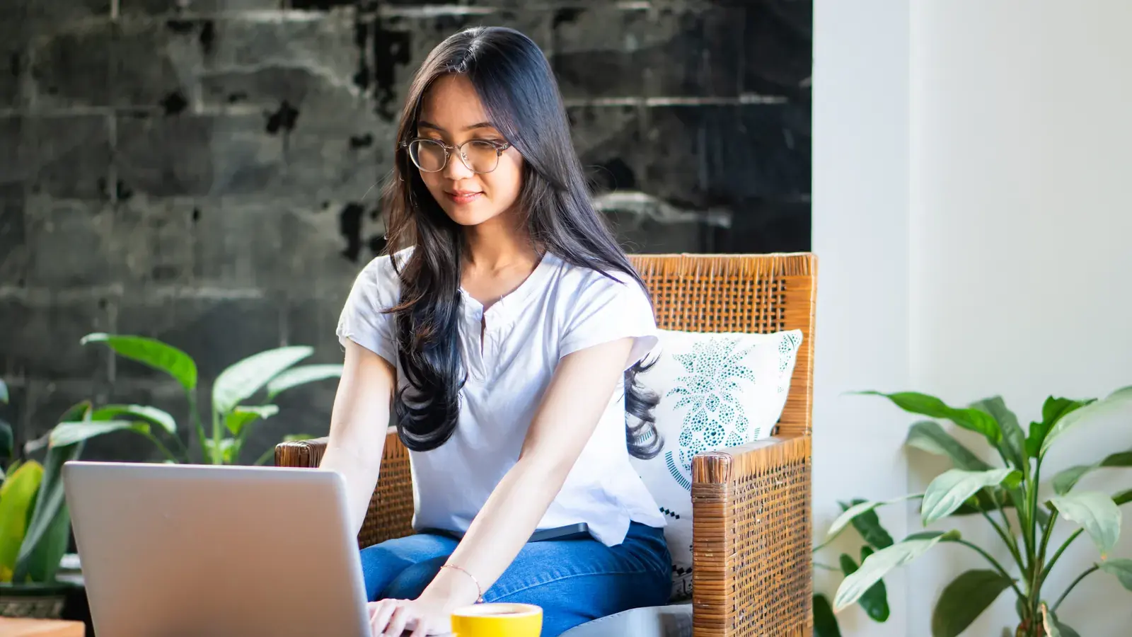 An Indonesian virtual assistant working at a laptop in a plant-filled home workspace.