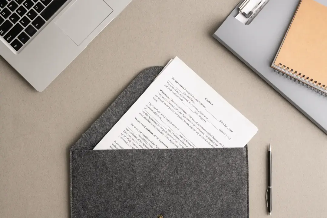 Dokumen kontrak, laptop, dan pulpen di meja.