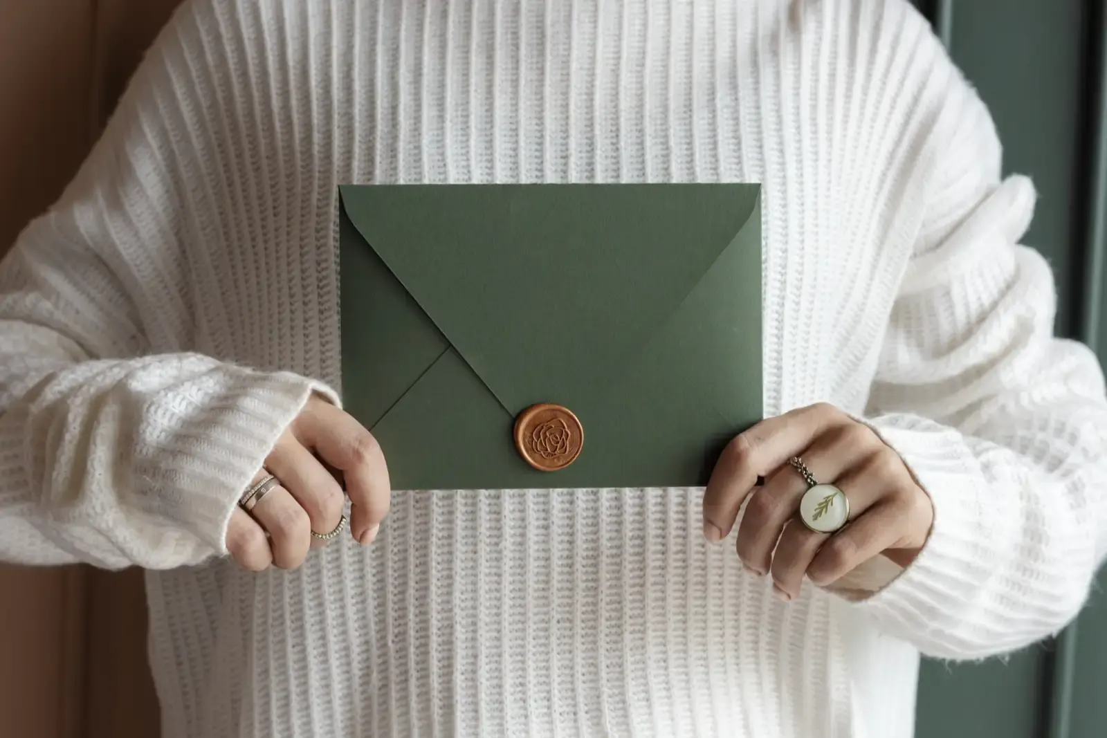 Elegant green envelope held in soft white sweater.