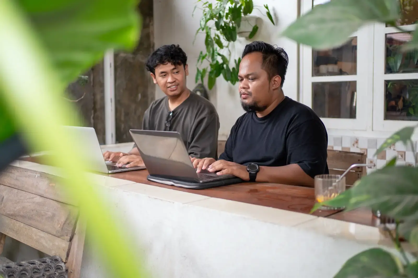Indonesian men working on laptops at cafe outdoor.