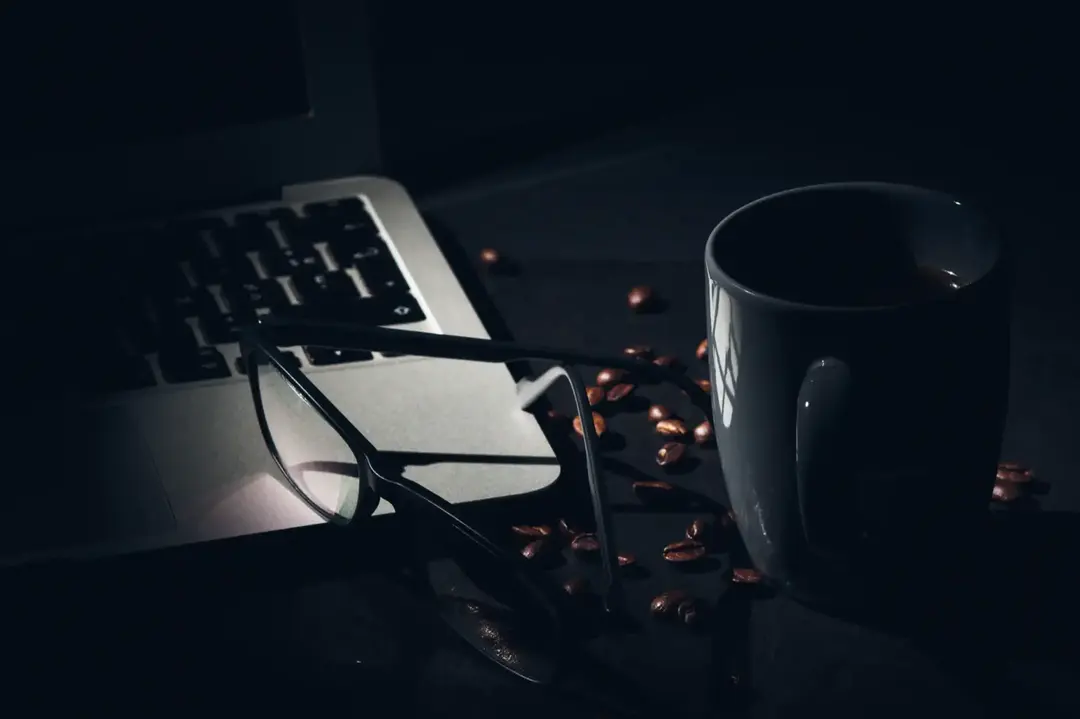Laptop, kopi, dan kacamata di meja.